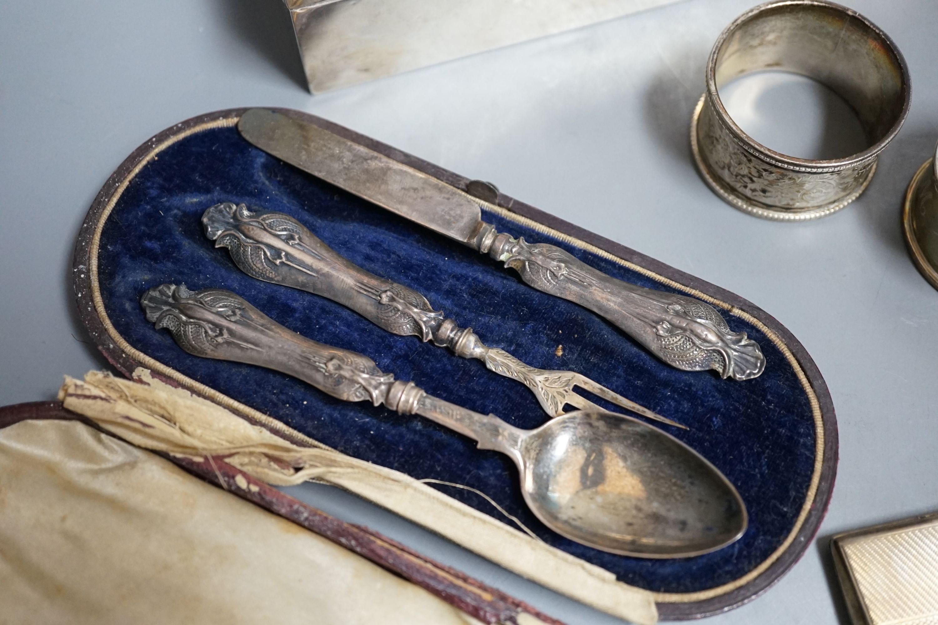 Sundry silver items including a George V 'The Gift of the Goldsmiths Company' box by Garrard & Co, London, 1926, 92mm, a silver cigarette case and box, four silver napkin rings, a cased silver christening trio and a silv